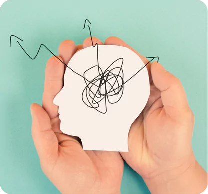 a pair of hands gently holding a cut-out silhouette of a human head, which is white and positioned against a light blue background. Inside the silhouette, there is a scribbled, tangled line representing a chaotic or confused thought process. From this scribble, three arrows extend outward, suggesting the idea of thoughts or ideas emerging from the confusion. The overall theme of the image seems to convey mental health issues