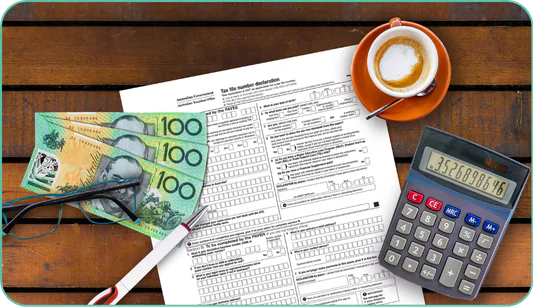a wooden table with several items on it. There is a tax form in the center, titled "Tax file number declaration." On top of the form, there are three Australian 100-dollar bills, a pair of reading glasses, and a pen. To the right of the form, there is a calculator displaying the number 35268986.46. In the top right corner, there is a cup of coffee on a saucer.